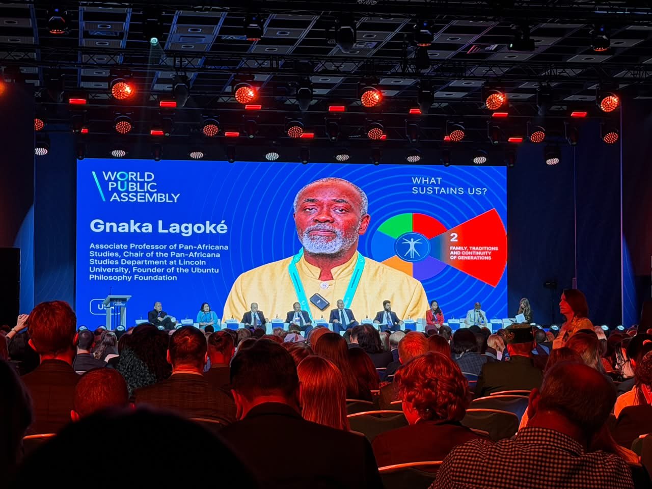 Dr. Gnaka Lagoke on the main screen during a World Public Assembly panel in Moscow, seen from the audience